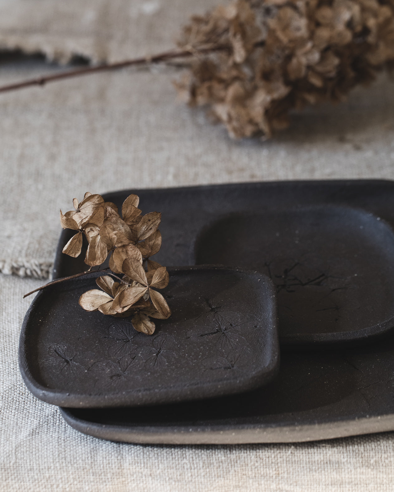 Handmade matte black small rectangular plates with hydrangea flower imprints, handmade by clay beehive ceramics.