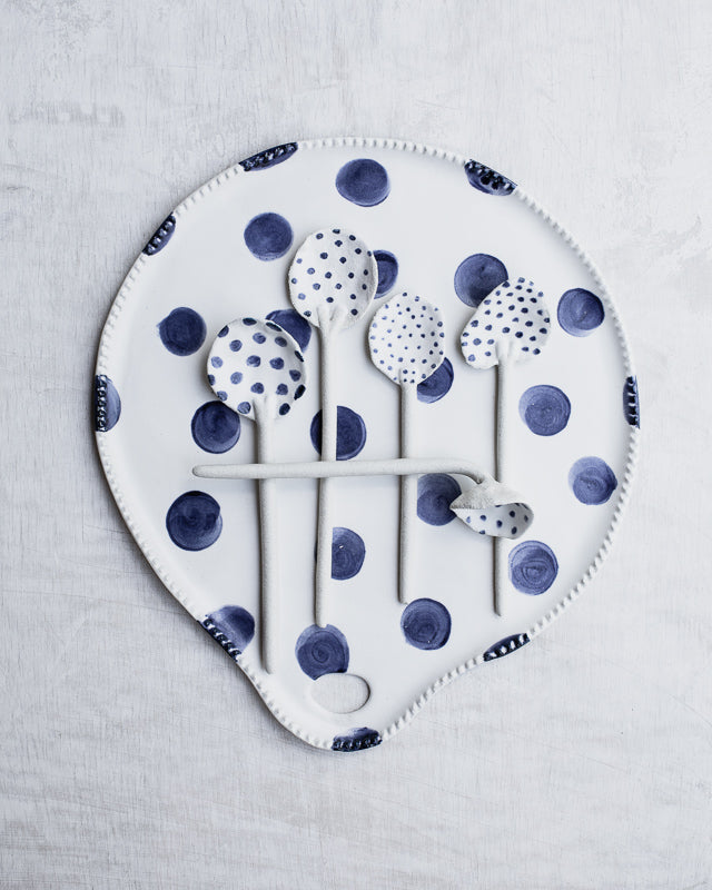 ceramic hand made spoons with spots sitting atop a spotty ceramic platter in blue and white